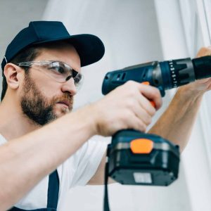 adult repairman in goggles fixing window handle by electric drill.jpg