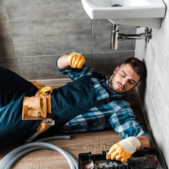 bearded handyman lying on floor near toolbox in bathroom.jpg